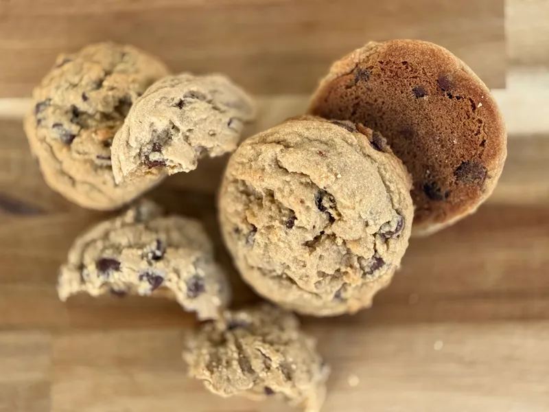 Chocolate chip cookies piled on a wooden board, seen from above, two of them broken open
