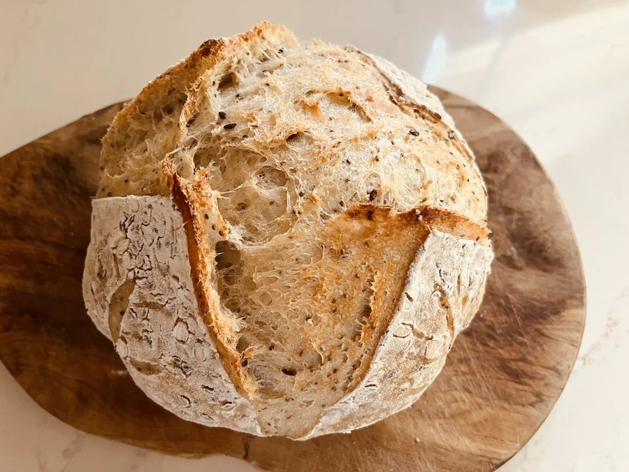 A round, flour-dusted sourdough loaf with a scored top, sitting on a wooden board