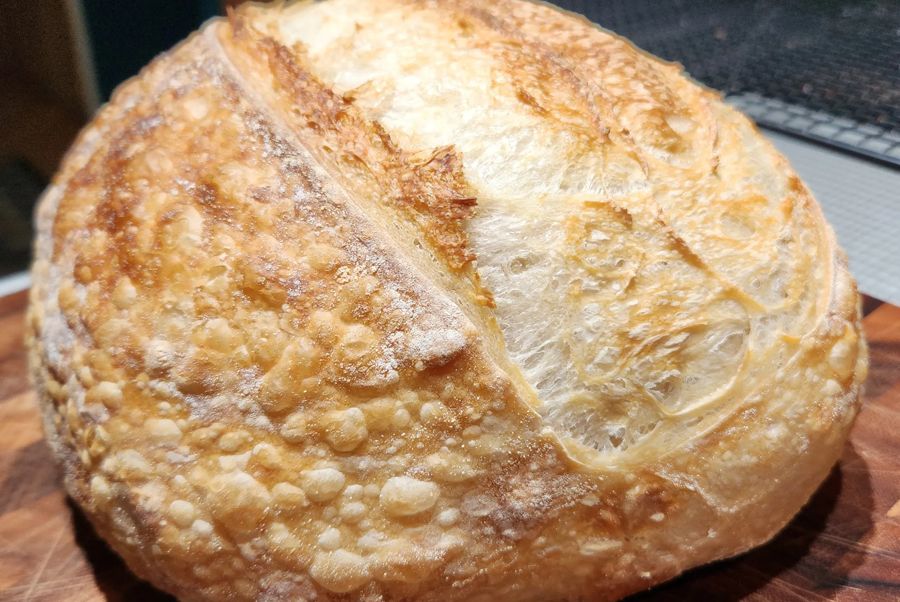 A round sourdough loaf with a golden, blistered crust and one long score, on a wooden board